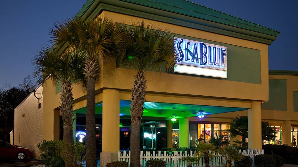 Exterior view of SeaBlue with blue green roof and tan exterior plus a large blue neon sign on the front of the building in Myrtle Beach, South Carolina, USA