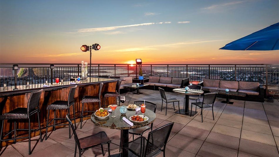 VUE Rooftop Bar with black chairs and tables, one set with food, and a beautiful sunset over the river in the French Quarter in New Orleans, Louisiana, USA