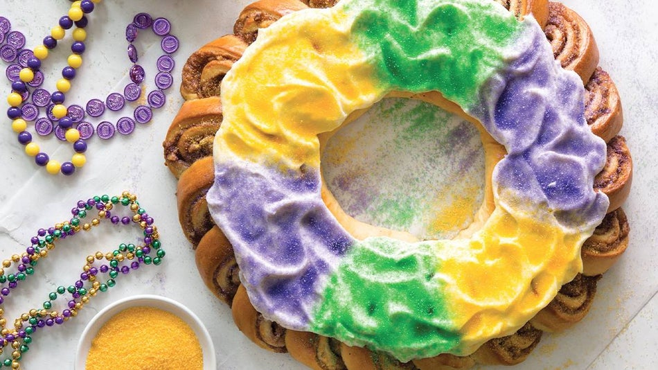 Close up of a King Cake with yellow, green and purple sprinkles and Mardi Gras beads to the left of the cake in New Orleans, Louisiana, USA
