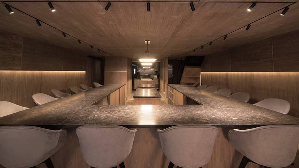 Close up of an empty bar with a grey county top and grey seating with small lights overhead pointing down at Atomix in NYC, New York, USA