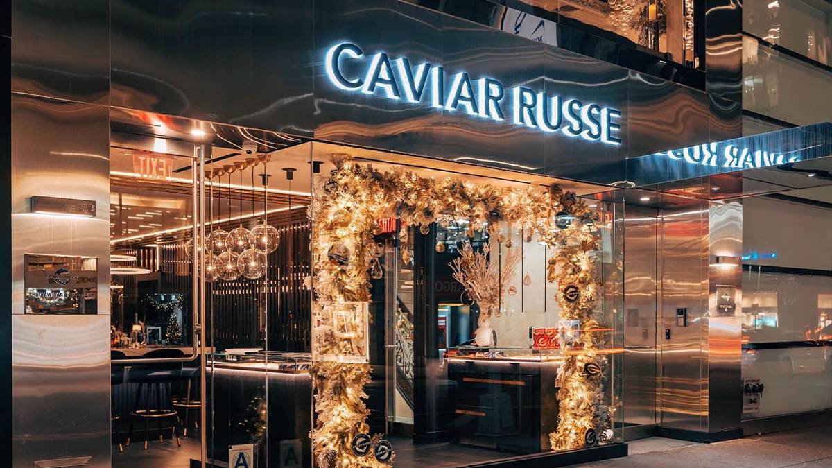 Close up photo of the entrance of Caviar Russe, large glass windows and door decorated with yellow lights and a glowing sign that says Caviar Russe above the door in NYC, New York, USA