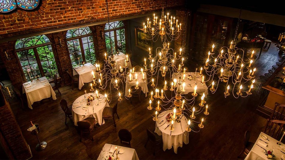 View looking down over One If By Land, Two If By Sea, with several tables with white cloths and flowers in the center and five big gold chandeliers handing from the ceiling in NYC, New York, USA