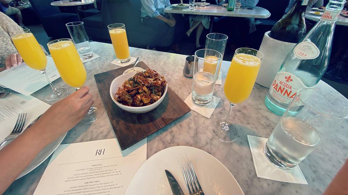 Close up of a marble table with several mimosas on it and an appetizer along with some menus at RH Rooftop Restaurant New York in NYC, New York, USA