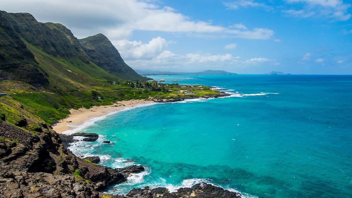 Rocky shoreline and pocket beach at Makapu'u Point on a sunny day with bright blue water in Oahu, Hawaii, USA