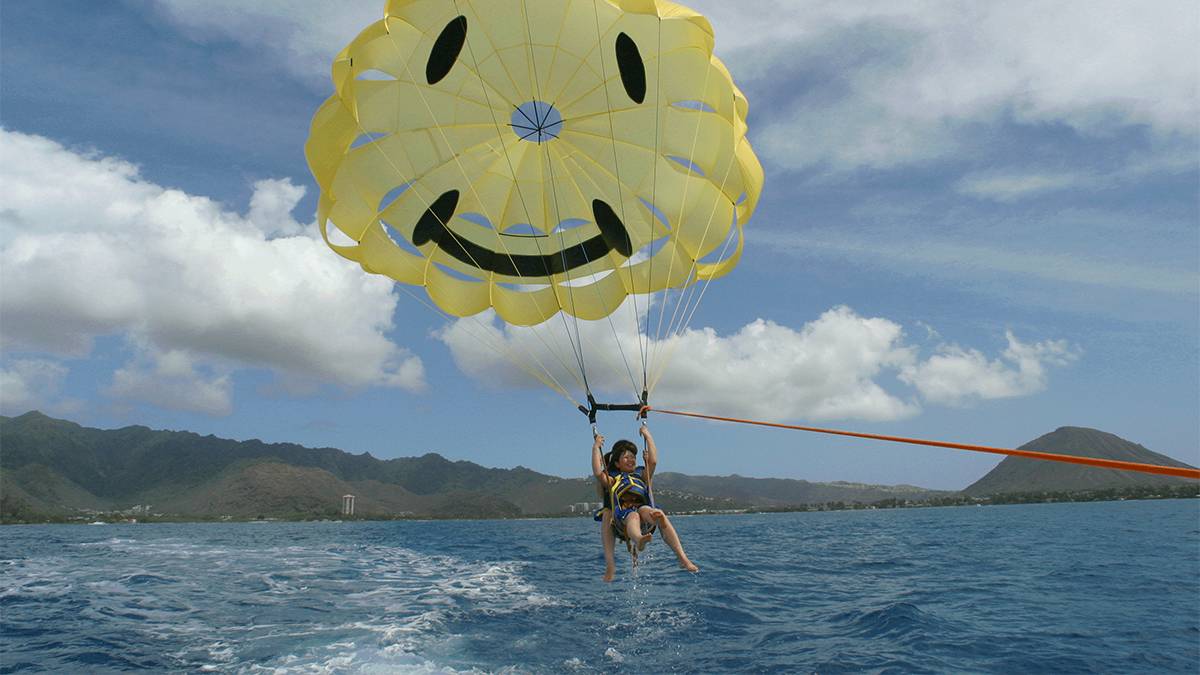 Two women parasailing with a chute that is a yellow smiley face at Parasailing Oahu in Oahu, Hawaii, USA