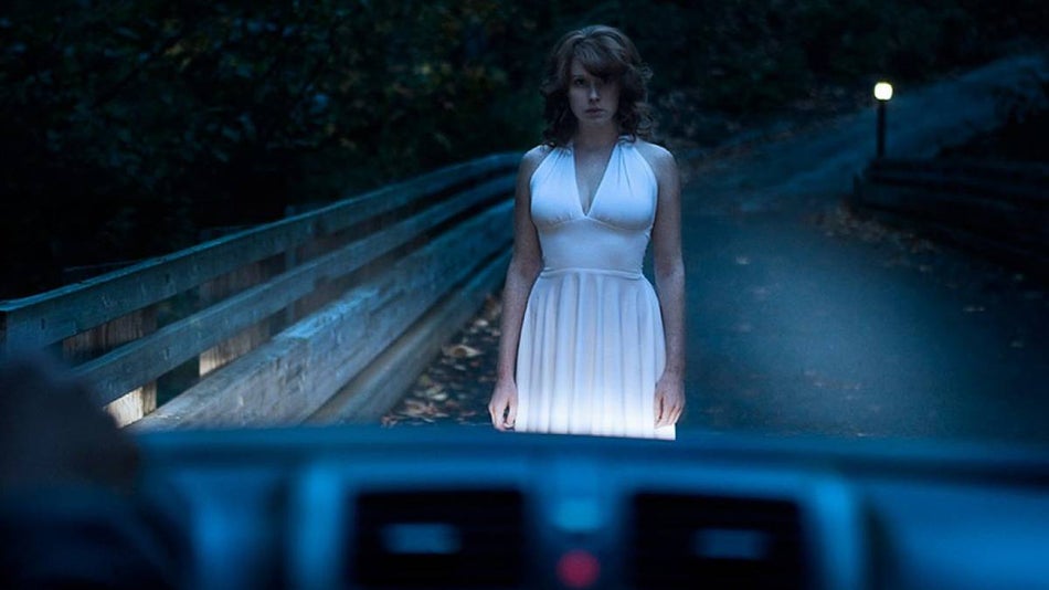 woman in white dress standing on a dark road in front of a car at Haunted Road in Orlando, Florida, USA