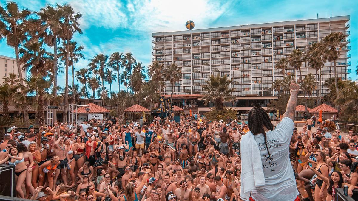 A large cowd of people in their swim suits on spring break looking up at the stage at Beach Bash Music Fest with a building and palm trees in the back ground in Panama City, Florida, USA