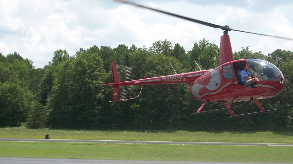A red and grey helicopter from Sevier County Aviation Helicopter Tours taking off into the air in Pigeon Forge, Tennessee, USA