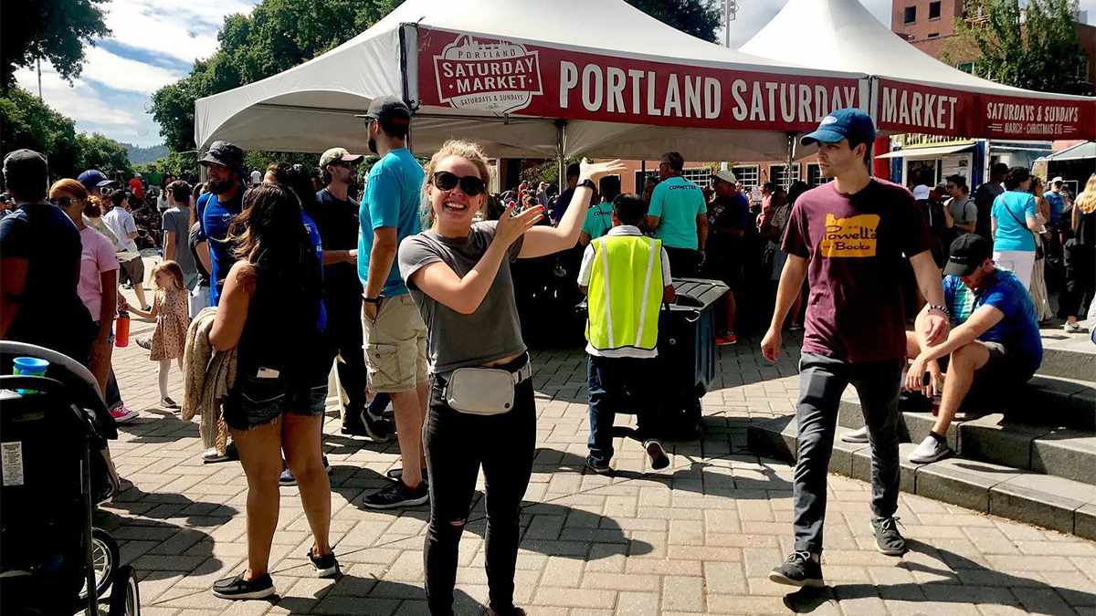Ground view of the busy Portland Saturday Market with a women in sunglasses pointing at the sign in Portland, Oregon, USA