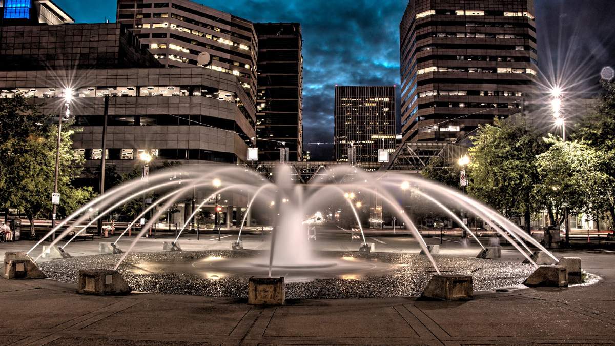 Close up of the Salmon Street Springs fountain at night with city buildings and lights in the background in Portland, Oregon, USA
