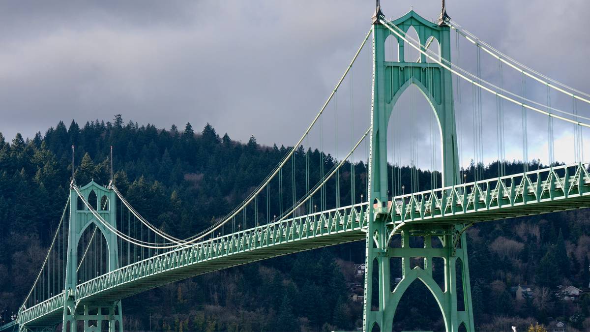 Wide shot of St. Johns Bridge from the side on a cloudy day with forrest in the background in Portland, Oregon, USA