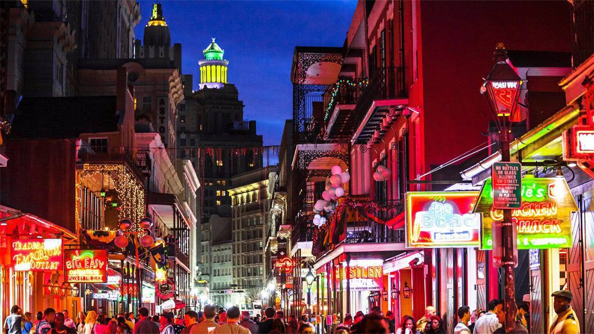 crowd walking around street with various establishments with neon signs at night at French Quarter in New Orleans, Louisiana, USA