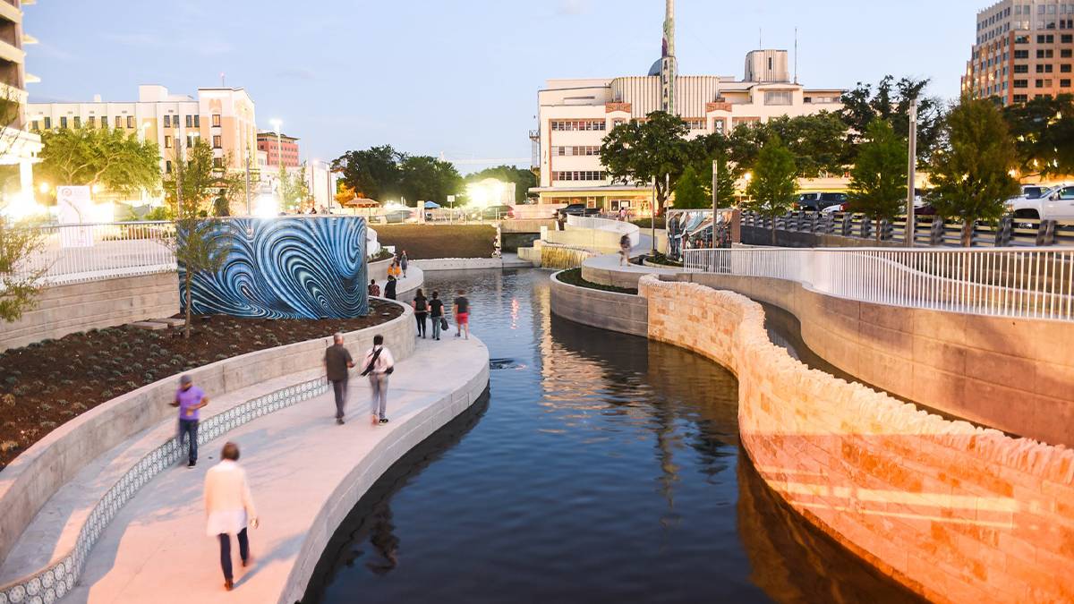 View looking down at people walking next to the water with stone walls and a blue mural at San Pedro Creek Culture Park in San Antonio, Texas, USA