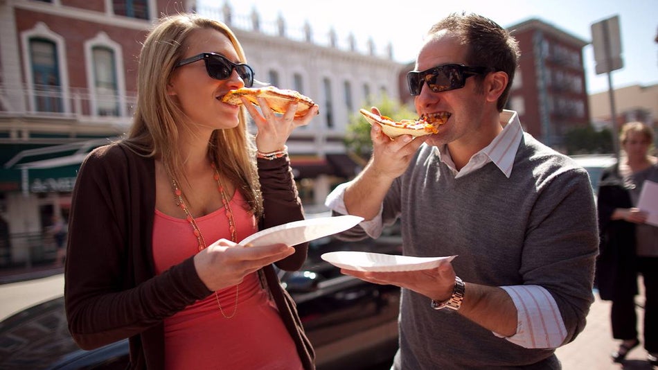 A man and a woman in sun glasses eating pizza on the Brothels, Bites, and Booze Food Tour in San Diego, California, USA