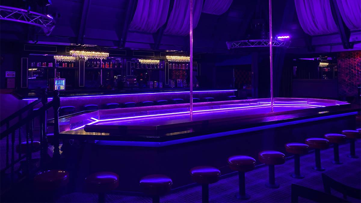View of a strange with bar stools surrounding it and two poles going up to the ceiling with a bar in the background with purple lights at Cheetah’s Gentlemen Club in San Diego, California, USA