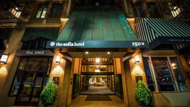 View of entrance to the Sofia Hotel, a yellow brick building with green accents and the light on at night in San Diego, Califonira, USA