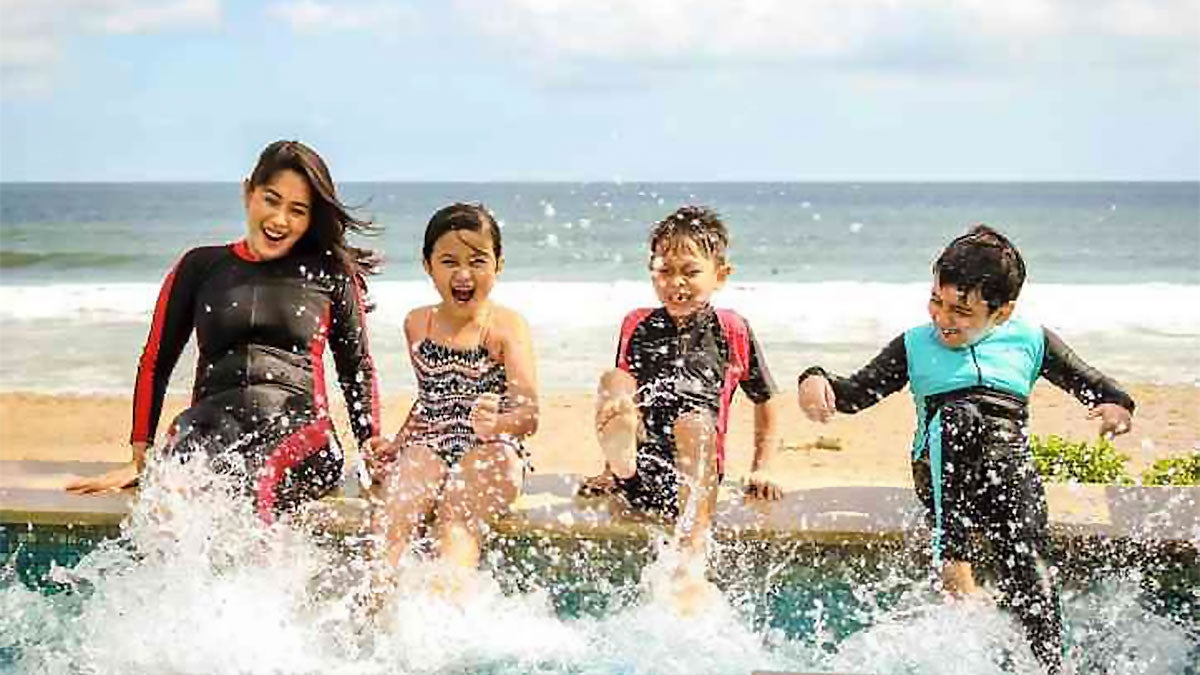 Family with kids sitting on a wall splashing their feet in the water in San Diego, California, USA