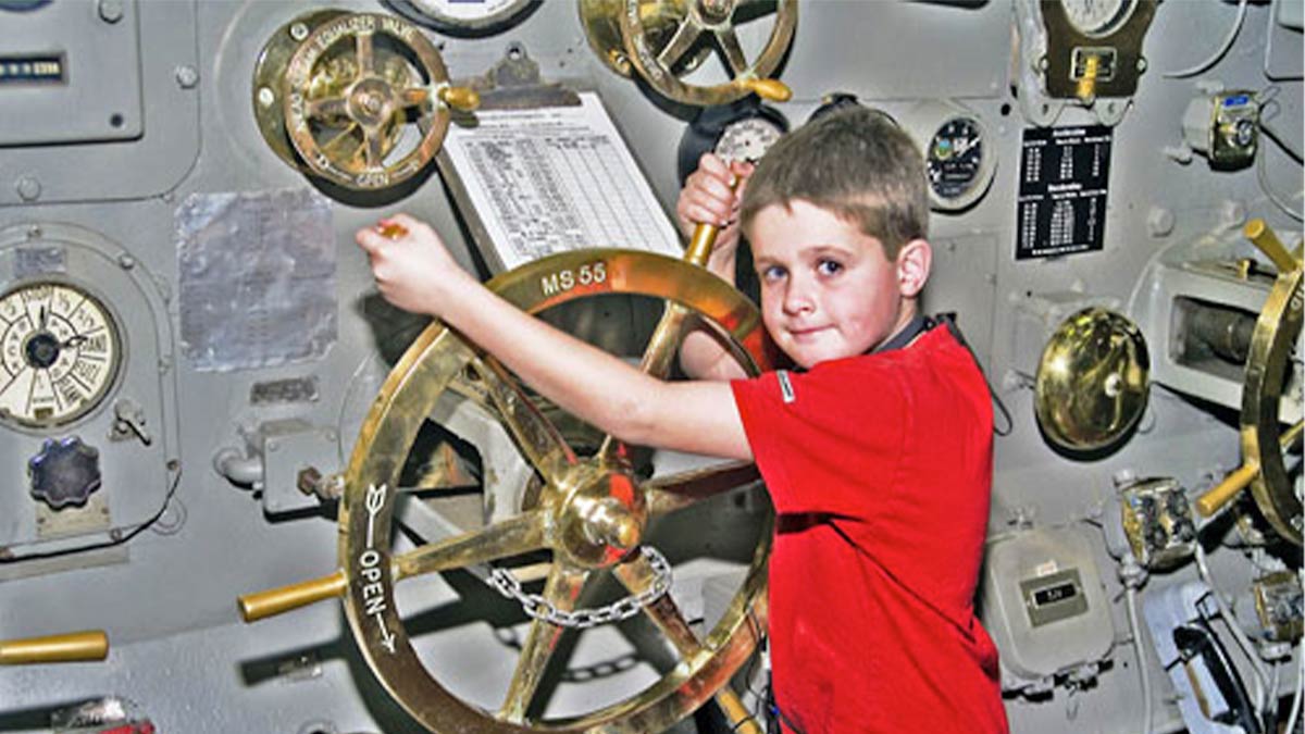 Boy holding on to a Gold Helm inside of the USS Midway Museum in San Diego, California, USA