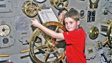 Boy holding on to a Gold Helm inside of the USS Midway Museum in San Diego, California, USA