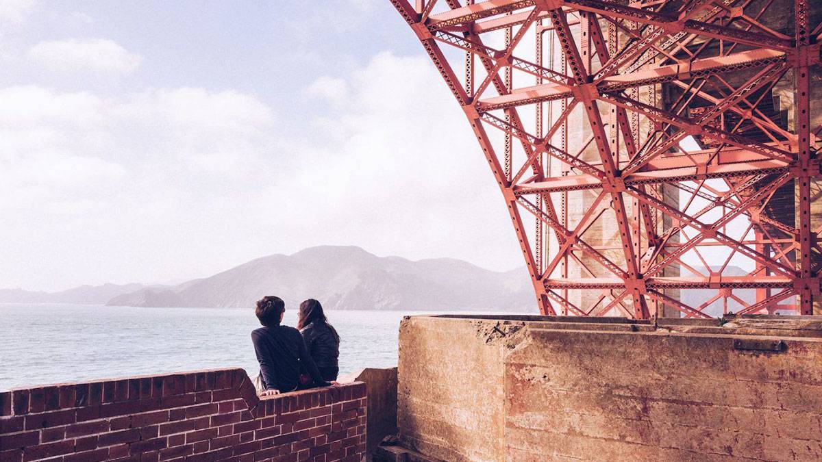 Couple sitting under Golden Gate Bridge overlooking the bay in San Francisco, California, USA