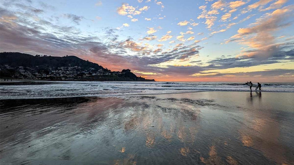 Wide shot of Pacifica State Beach at sunset with two surfers walking near the water in San Francisco, California, USA