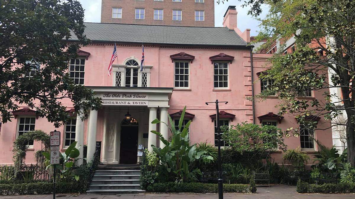 Wide shot of the Olde Pink House, the building is painted a faded light pink color and has lots of windows, restaurant and tavern on a sunny day in Savannah, Georgia, USA