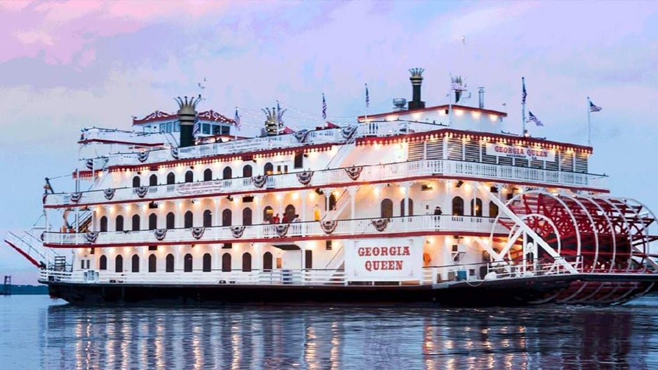 View of cruise boat the Georgia Queen with its lights on on the water and pink and purple sunset behind it as part of the Savannah Land & Sea Tour in Savannah, Georgia, USA