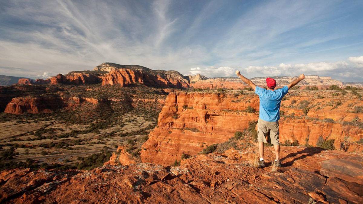 A hiker in Sedona, Arizona. Doe Mountain Trail. Middle Aged Caucasian male with arms raised against a dramatic sky. Self Portrait. Additional themes include backcountry, adventure, eco tourism, trail running, exercise, fitness, health, healthy living, recreation, leisure, one man, back view, and happiness.