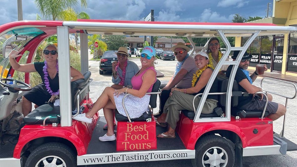 A group of people sitting in a large red golf cart smiling on the St. Augustine Wine and Dine Tour in St. Augustine, Florida, USA.