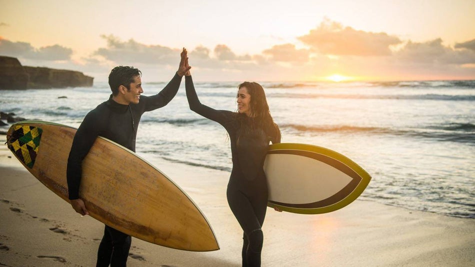 man and woman surfers high five on beach at sunset