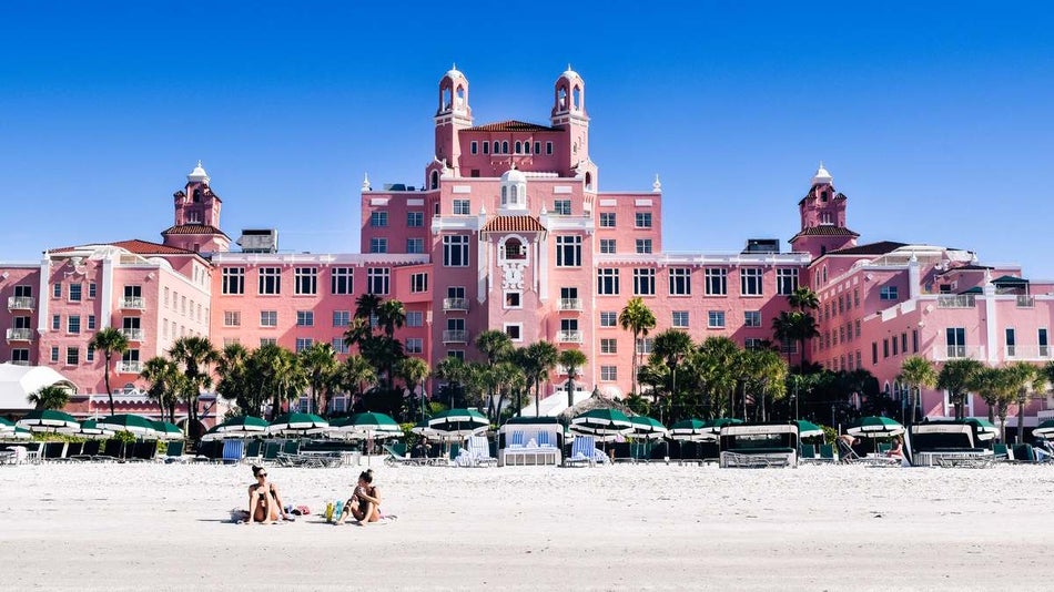 Two women on the beach with umbrella behind them and the massive pink Don CeSar behind them on a sunny day in Tampa, Florida, USA