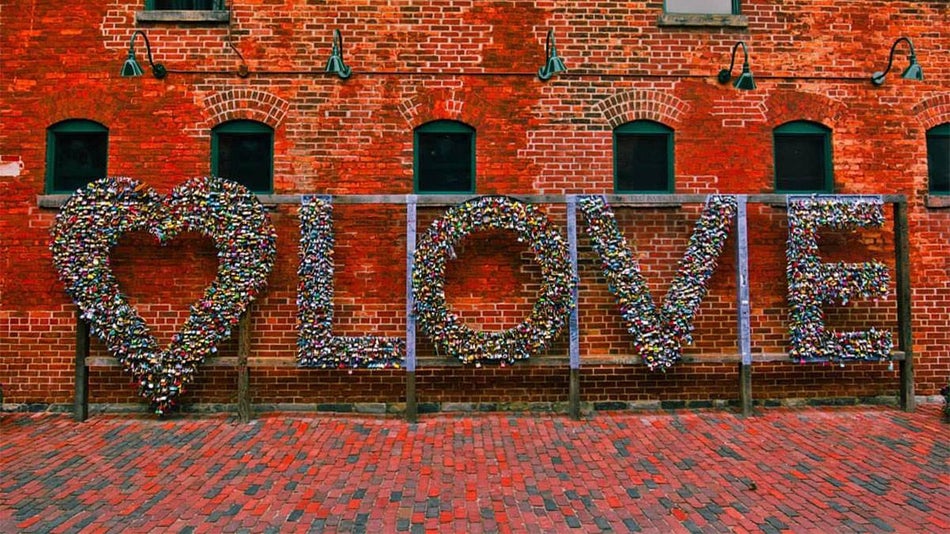 A bright red brick wall with a giant heart and the word "LOVE" spelled out in locks with a brick road in front of it at Distillery District Heart in Toronto, Ontario, Canada