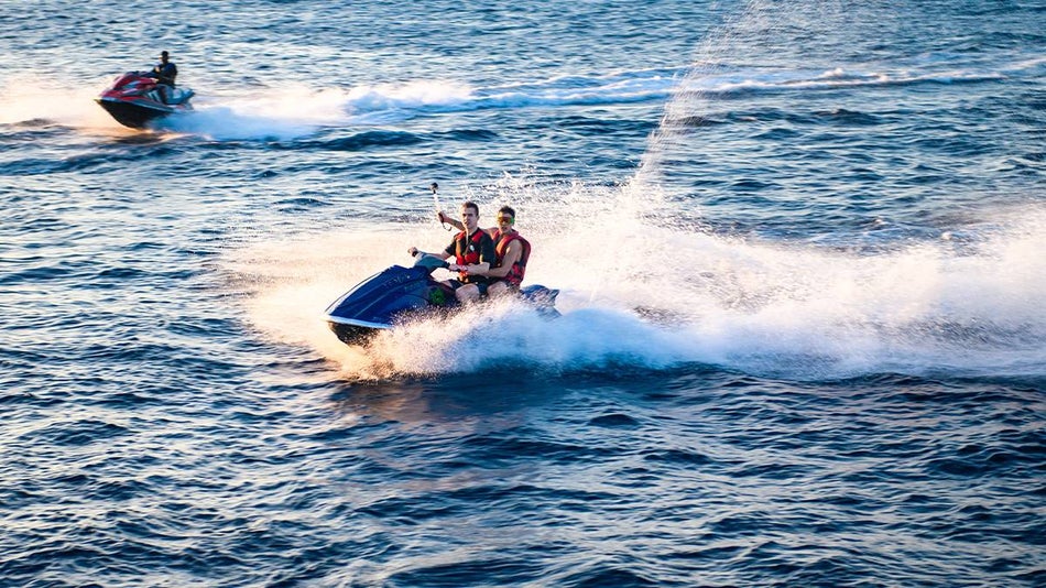 Two men on a jet ski driving in the ocean on a sunny day