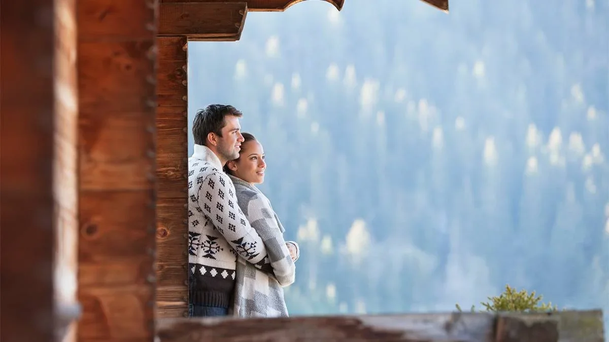 Couple in sweaters standing on the porch of their cabin