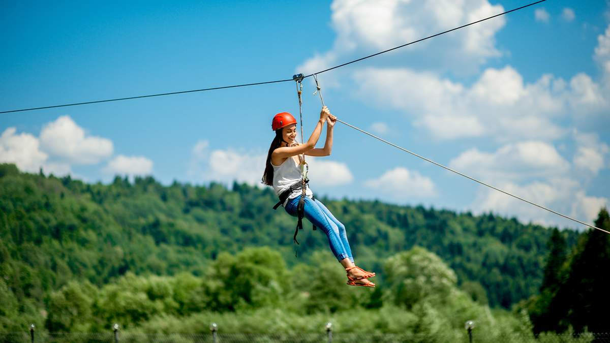 Woman in a red helmet ziplining on a sunny day.