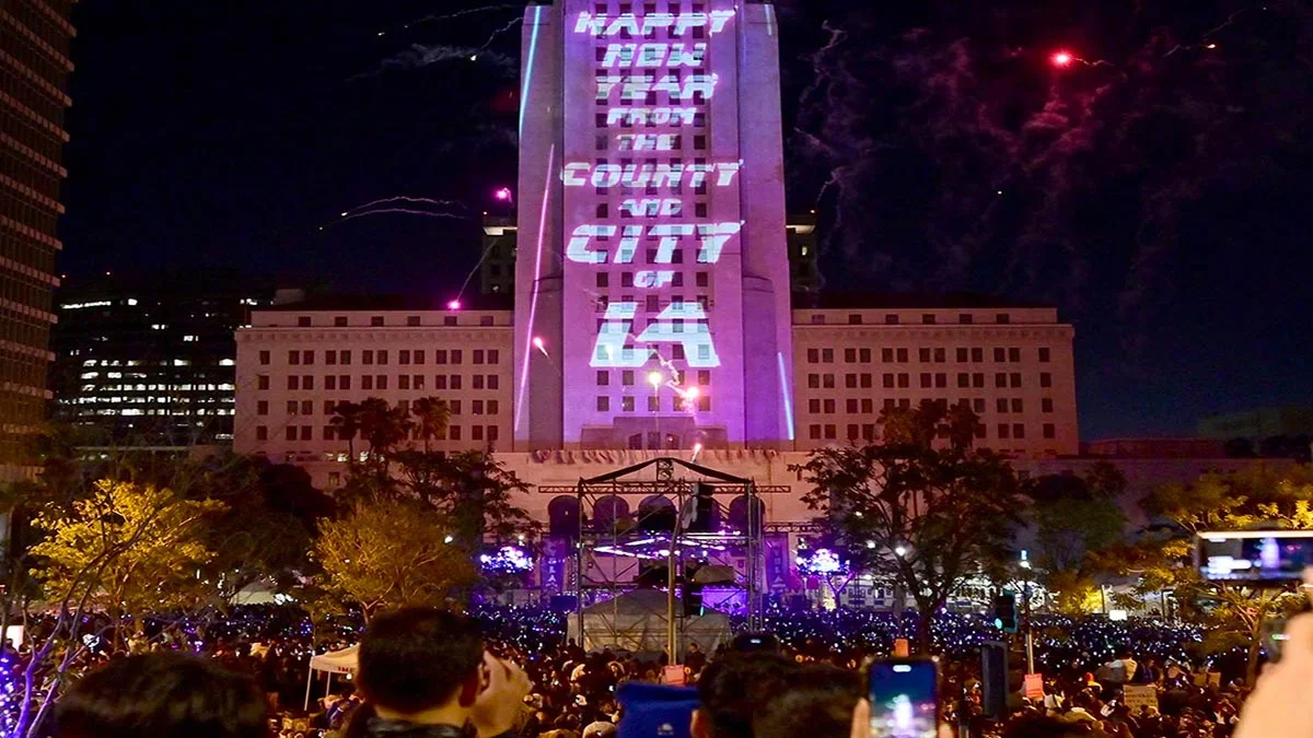 crowd taking photos of building lit up with words with fireworks in background at 2022 Grand Parks NYELA in Los Angeles, California, USA