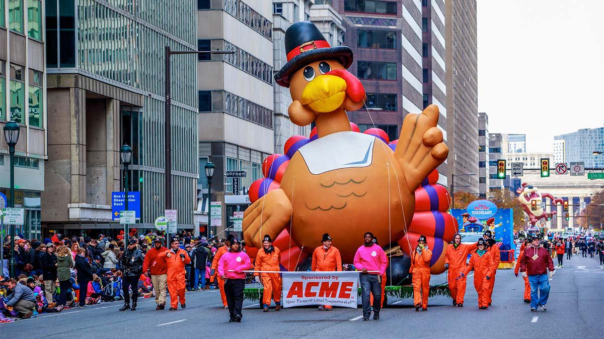 people walking in parade with float with large inflatable turkey with crowd on the side watching at 6abc Dunkin Thanksgiving Day Parade in Philadelphia, Pennsylvania, USA