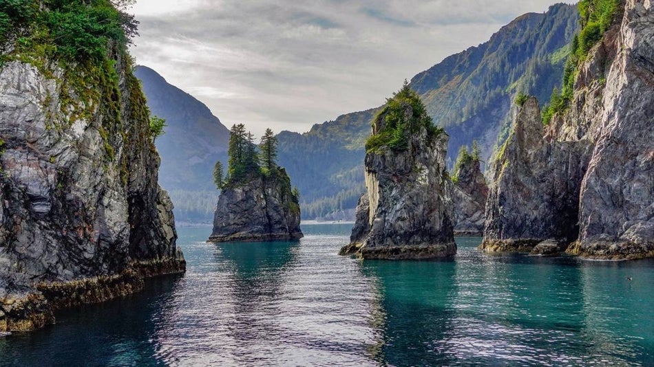 Tall rock formations coming out of clear blue water surrounded by mountains in Alaska