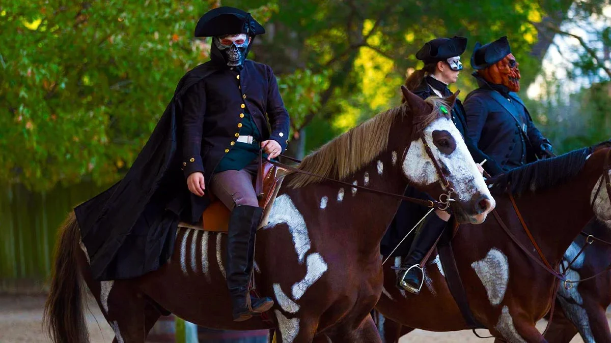One woman and two men are wearing different character face masks while riding a horse.
