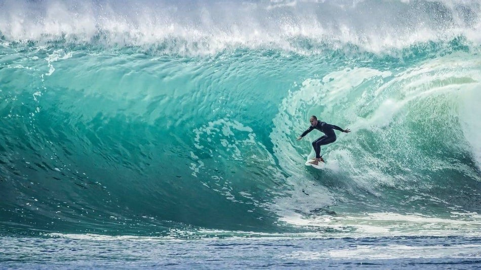 Surfer in black wet suit surfing along a Big blue tunnel Wave