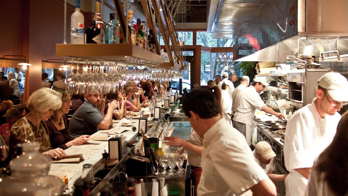 View of a busy kitchen and bar with a lot of people working and drink at Curate Tapas Bar in Asheville, North Carolina, USA