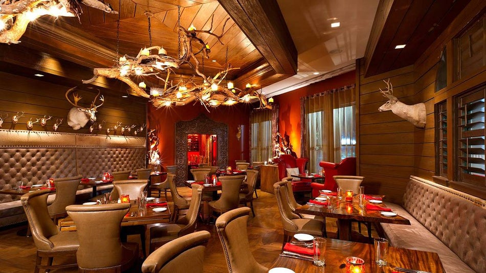 Wide shot of a wooden and red dining room with brown chairs and antlers as lighting fixtures and deer on the wall at Red Stag Grill in Asheville, North Carolina, USA