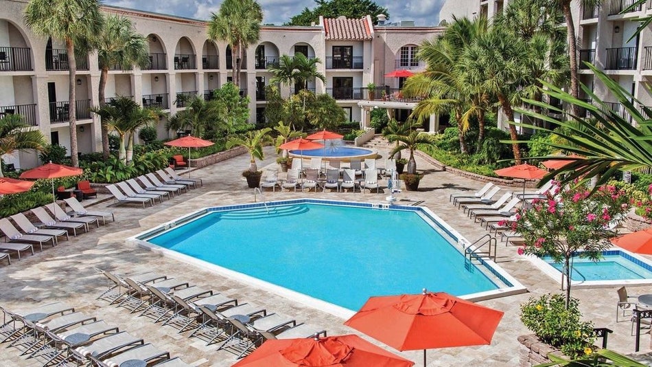Outdoor pool surrounded by sun lounge chairs with orange umbrellas and palm trees at the Wydham Hotel Boca Raton