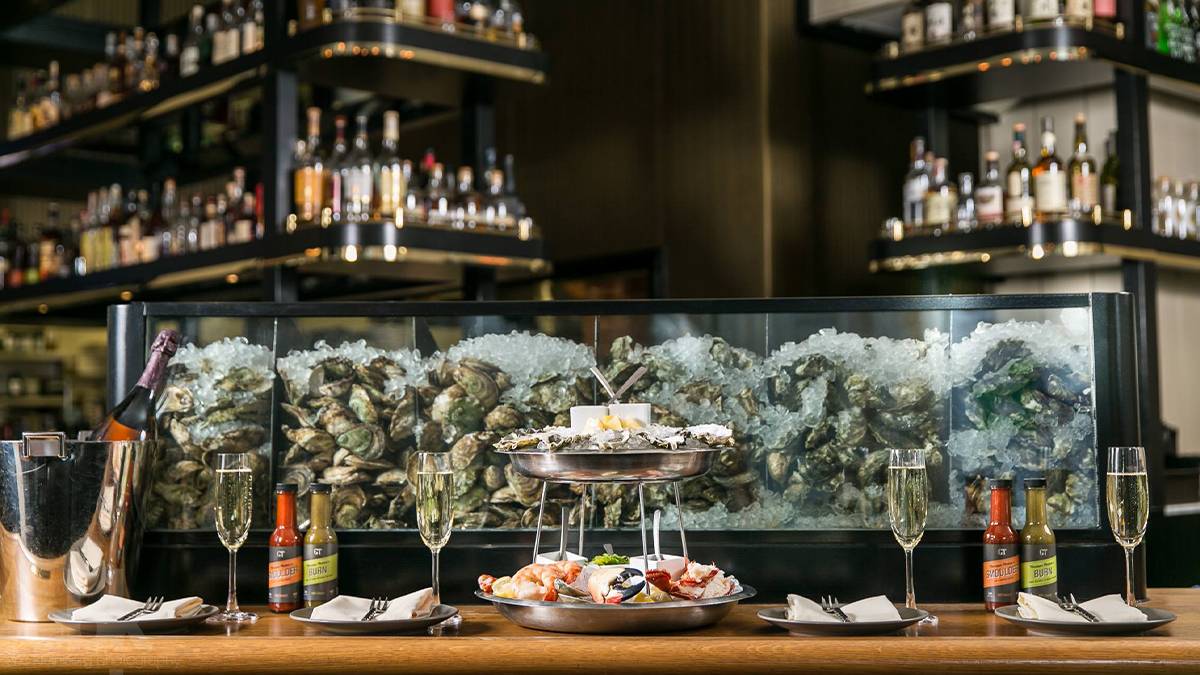 Close up photo of oysters on ice in a glass tank with drinks and a tray of oysters in front it at GT Fish & Oyster in Chicago, Illinois, USA