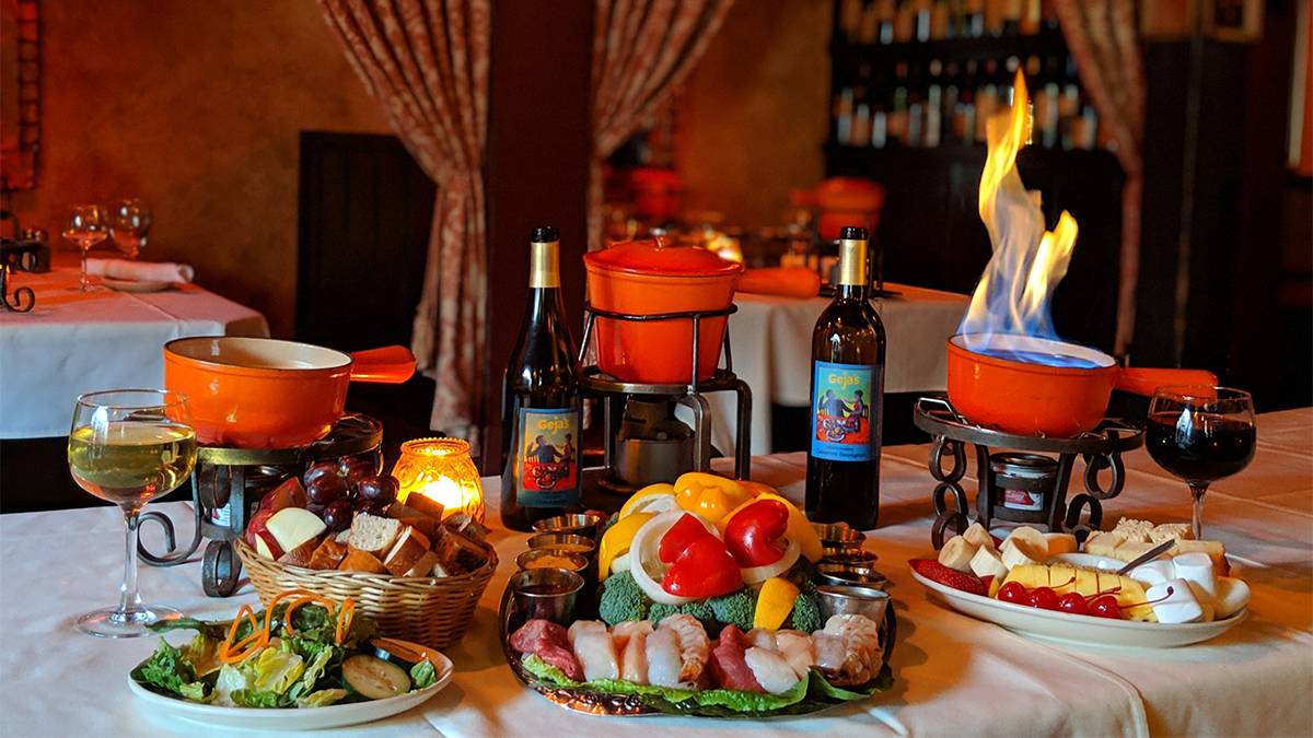 Close up photo of a three fondue pots with lots of different things to dip in them and two bottles of wine at Geja’s Cafe in Chicago, Illinois, USA