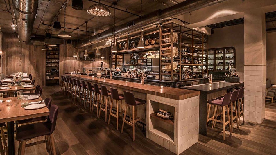 Wide shot of the bar and dining room with wooden counter top and tables and a large shelving area behind the bar at Monteverde in Chicago, Illinois, USA