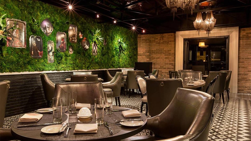 Dining area with black leather tables and chairs and a wall covered in moss with different shaped portraits on it at Boke in Chicago, Illinois, USA