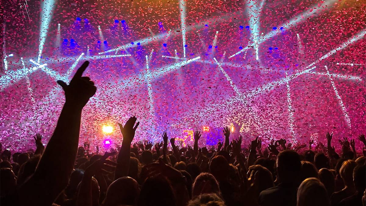 live concert on stage with white purple and blue lights with crowds hands in the air