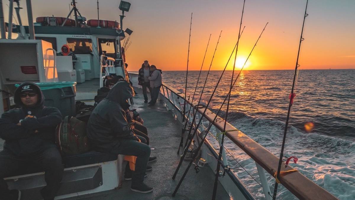 deep sea fishing boat with peple sitting watching their fishing poles with the sunset into the ocean in the background
