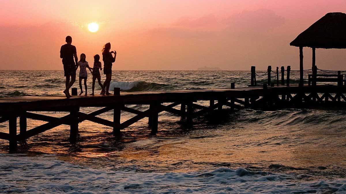 family standing on pier over beach at sunset